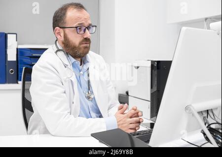 Arzt im Gespräch mit Online-Patienten auf Desktop-Computer-Bildschirm sitzen am Büro Schreibtisch der Klinik geben Online-Konsultation für häusliche Gesundheitsbehandlung. Telemedizinische Fernarztterminierung. Stockfoto