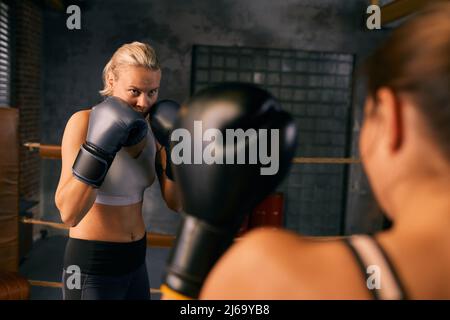 Horizontaler, über die Schulter gerichteter Schuss zweier junger Frauen, die mit dem Boxkampf beginnen Stockfoto