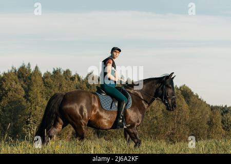 Teenager-Mädchen Reiten Bay Pferd im Feld. Stockfoto