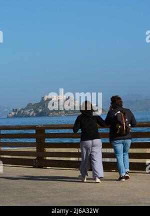Touristen genießen den Blick auf Alcatraz Island und das Alcatraz Gefängnis von einem Pier im Fisherman's Wharf-Viertel von San Francisco, Kalifornien. Stockfoto