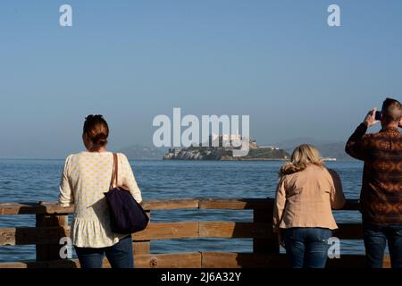 Touristen genießen den Blick auf Alcatraz Island und das Alcatraz Gefängnis von einem Pier im Fisherman's Wharf-Viertel von San Francisco, Kalifornien. Stockfoto