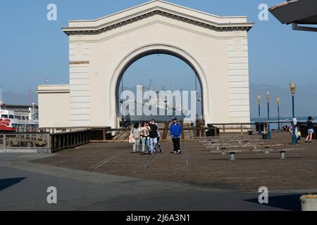 Touristen besuchen den historischen Pier 43 in San Francisco mit dem Freiheitsschiff der SS Jeremiah O'Brien aus dem 2. Weltkrieg, das heute in San Francisco liegt, in der Ferne. Stockfoto