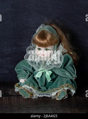 Erstaunlich realistische Vintage Puppe mit grünen Augen. Die Puppe in einem grünen Kleid mit Spitze gekleidet. Selektiver Fokus. Porzellan. Stockfoto