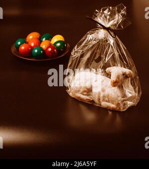 Osterlammkuchen in transparenter Verpackung und Eier auf braunem Hintergrund, Stockfoto Stockfoto