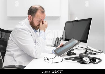 Der junge Arzt reibt sich die Augen, fühlt sich müde und unglücklich. Konzept für Stress und Frustration im Gesundheitswesen. Hochwertige Fotografie Stockfoto