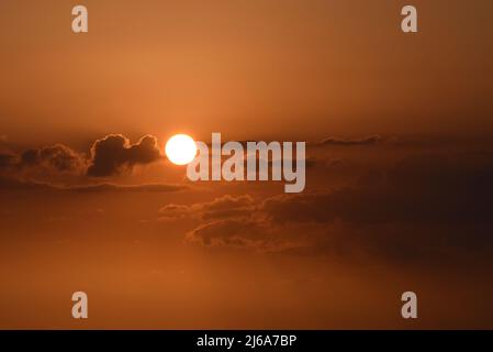 Wolken, die vor der Sonne vorbeiziehen, erzeugen bei Sonnenuntergang einen dramatischen Himmel. Stockfoto