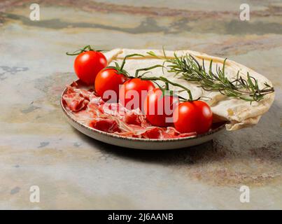 Teller mit Prosciutto parma, Tomaten, Rosmarin und ungesäuertem Fladenbrot auf Holzboden, italienisches Frühstück, Stockfoto Stockfoto