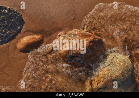 Direkt über dem Bild der kleinen Wellen, die in den Strand Rollen, übersät mit bunten Felsen und Felsbrocken Stockfoto