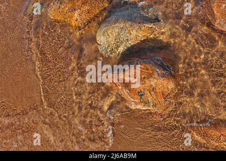 Direkt über dem Bild der kleinen Wellen, die in den Strand Rollen, übersät mit bunten Felsen und Felsbrocken Stockfoto