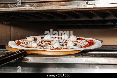 Der Prozess der Zubereitung von Pizza durch den Koch. Italienische Pizza mit Schinken, Käse, Mozzarella im Ofen in einem traditionellen Restaurant Stockfoto
