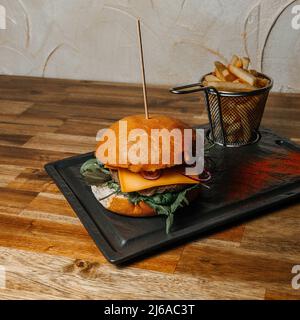 Rindfleisch-Burger mit frischem Salat, Zwiebeln, Ruccola, Tomaten, Käse und pommes auf einem Holztisch, Stockfoto, italienisches Küchenkonzept Stockfoto