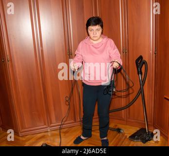 Eine Frau mittleren Alters sammelt einen Staubsauger für die Hausreinigung. Stockfoto