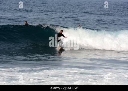 Ein männlicher Surfer im Nassanzug, der am Strand Playa del Socorro in Los Realejos, an der Nordküste von Teneriffa, Kanarische Inseln, Spanien, eine Welle surft. Stockfoto