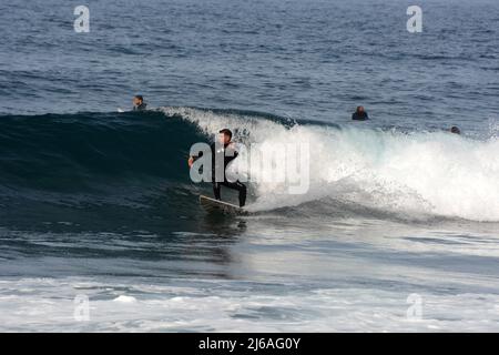 Ein männlicher Surfer im Nassanzug, der am Strand Playa del Socorro in Los Realejos, an der Nordküste von Teneriffa, Kanarische Inseln, Spanien, eine Welle surft. Stockfoto