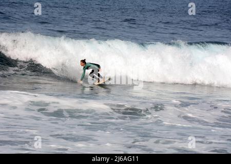 Eine Surferin im Nassanzug, die am Strand Playa del Socorro in Los Realejos, an der Nordküste von Teneriffa, Kanarische Inseln, Spanien, eine Welle surft. Stockfoto