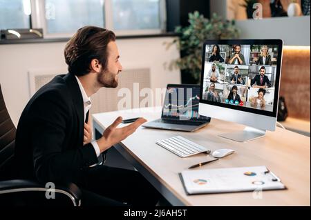 Brainstorming der Gruppe durch Videoanruf. In seinem modernen Büro sitzt ein erfolgreicher kaukasischer männlicher Aktienmakler, spricht mit Kollegen auf einer Videokonferenz, erarbeitet eine Krypto-Strategie und diskutiert Risiken Stockfoto