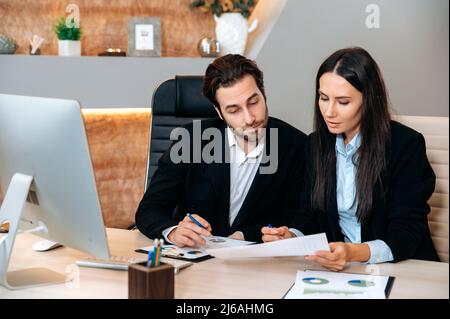 Kaukasische Mitarbeiter arbeiten in modernen Büros zusammen. Einflussreiche männliche und weibliche Mitarbeiter diskutieren über Ideen für Projekte und betrachten Finanzdiagramme. Business Partners Brainstorming gemeinsam Stockfoto