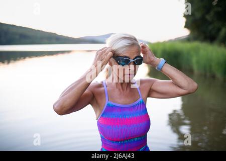 Porträt einer aktiven älteren Schwimmerin im Freien am See. Stockfoto