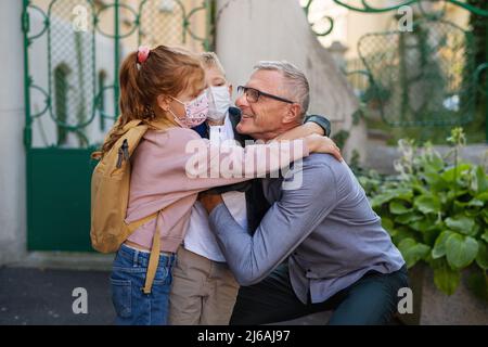 Glücklicher Großvater, der Enkel von der Schule nach Hause bringt und draußen auf der Straße vor der Schule wartet. Stockfoto