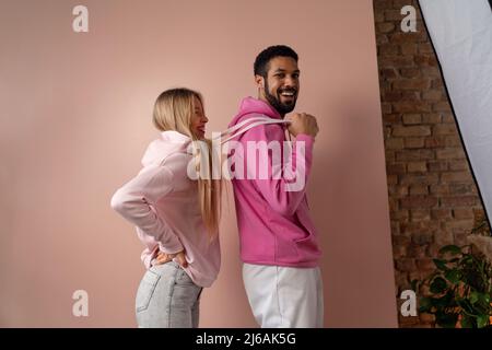 Fashion Studio Portrait eines glücklichen jungen Paares in Hoodie posiert auf rosa Hintergrund. Stockfoto