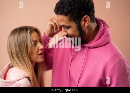 Fashion Studio Portrait eines glücklichen jungen Paares in Hoodie posiert auf rosa Hintergrund. Stockfoto