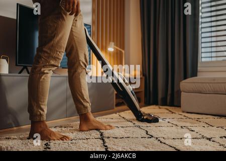 Lowsection of man Hoovering Teppich with Vacuum Cleaner in Wohnzimmer Stockfoto