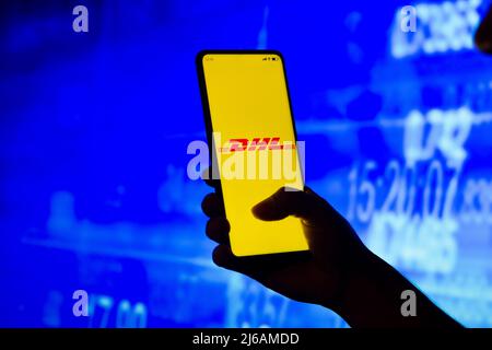 In dieser Abbildung hält eine Frau mit Silhouetten ein Smartphone mit dem DHL-Logo auf dem Bildschirm. Stockfoto