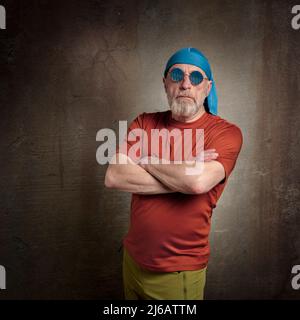 Porträt eines älteren, gutaussehenden Mannes mit grauem Bart in Totenkopf-Mütze und runder blauer Sonnenbrille, grunge städtische Umwelt Stockfoto
