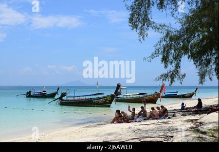 KRABI, THAILAND - 24. März 2022 : Touristen in einem Bikini sitzen auf der Insel Koh Poda, Provinz Krabi, Thailand, mit einem Smartphone im Schatten eines Baumes Stockfoto