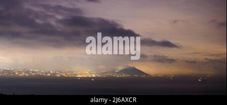 Dramatische Wolken über Küstenstadt und Hügel bei Nacht Stockfoto