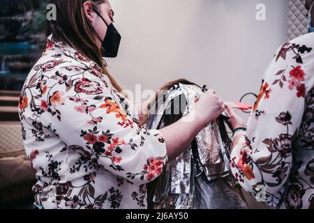 Die Frau färbt ihre Haare in einem Friseurladen, dem Prozess des Färbens ihrer Haare mit Folie. Stockfoto