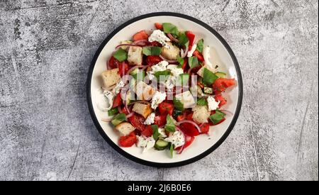 Toskanische Panzanella, traditioneller italienischer Salat mit Tomaten und Brot. Vegetarischer Panzanella-Salat auf einem runden Teller auf dunkelgrauem Hintergrund. Draufsicht Stockfoto
