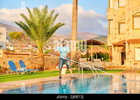 Mann, der den Außenpool putzt, schöne Aussicht auf die Natur im Hintergrund Stockfoto