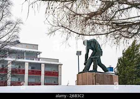 Rovaniemi, Finnland - 18.. März 2022: Bronzestatue eines Holzfällers, der an einem verschneiten Tag in Rovaniemi, Finnland, einen Baumstamm entbellt. Stockfoto