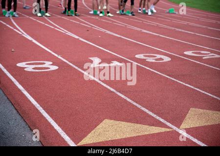 Läufer stehen an der Startlinie auf einer athletischen Rennstrecke in der Nähe von Rennbahnmarkierungen und Zahlen, die im Freien mit Kopierraum aufgenommen wurden. Stockfoto