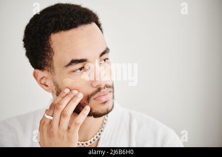 Hübscher bärtiger Mann, der Augenflecken auf sein auf weißem Hintergrund isoliertes Gesicht anwendet Stockfoto