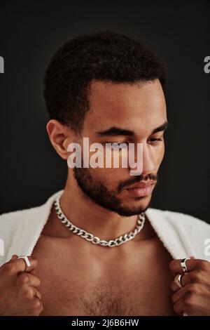 Nahaufnahme eines gutaussehenden metrosexuellen Mannes, der Augenflecken auf seinem Gesicht mit Accessoires auf seinem Hals und den Fingern vor dem schwarzen Hintergrund anlegt Stockfoto
