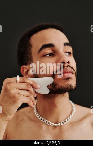 Bärtiger Mann mit Jade-Gesichtswalze für die Schönheits-Gesichtsmassagetherapie Stockfoto