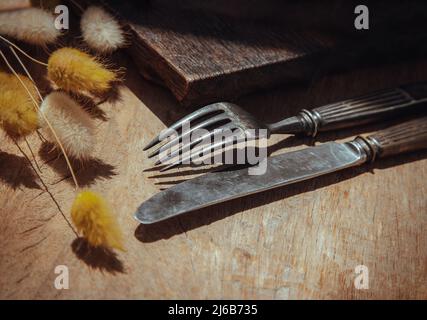 Vintage altes Metallmesser mit Gabel und getrockneten Kaninchen Schwanz Gras Blumen auf alten rustikalen Holztisch. Esskonzept, Kopierraum, selektiver Fokus. Stockfoto