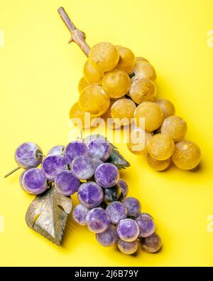 Zwei Trauben, eine gelbe und eine violette, beide aus Glas, auf gelbem Grund Stockfoto