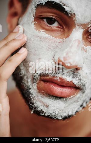 Nahaufnahme eines hübschen jungen Mannes, der kosmetische Maske auf sein Gesicht aufsetzte und die Kamera ansah Stockfoto