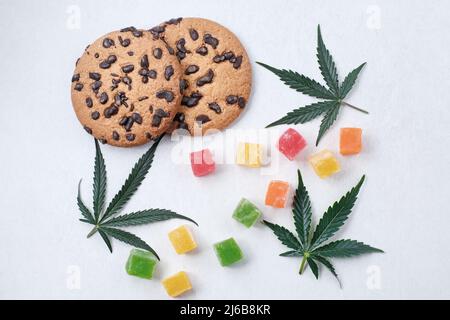 Amerikanische Cookies mit Cannabisextrakt. Süßigkeiten mit CBD-Öl. Marihuana Blätter auf weißem Hintergrund. Draufsicht, flach liegend. Stockfoto