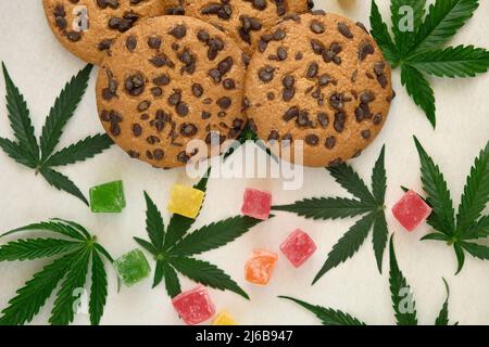 Amerikanische Cookies mit Cannabisextrakt. Süßigkeiten mit CBD-Öl. Marihuana Blätter auf weißem Hintergrund. Draufsicht, flach liegend. Stockfoto