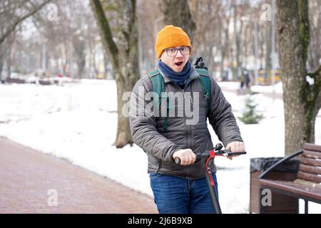 Der Typ fährt im Frühjahr im Park mit einem Elektroroller. Stockfoto