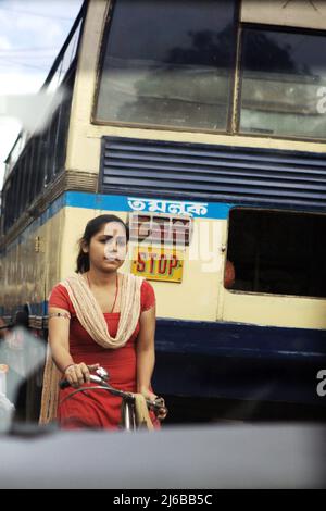 Eine Frau, die auf einer überfüllten Straße in Tamluk, Purba Medinipur, Westbengalen, Indien, Fahrrad reitet. Stockfoto