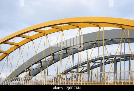 Drei Stahlbogenbrücken liegen nebeneinander und überspannen einen Fluss. Eine der Brücken ist auffallend gelb und die einzige Hängebrücke. Der t Stockfoto