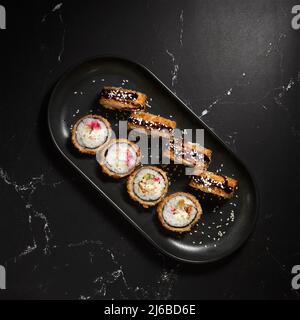 Heiß gebratene Sushi-Rollen und Maki mit Garnelen, Tempura Ebi auf schwarzem Stein, selektiver Fokus. Japanische Küche. Frittiert. Sushi-Menü. Nahaufnahme Stockfoto