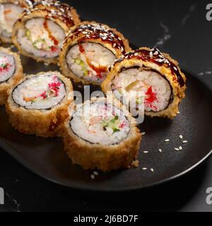 Heiß gebratene Sushi-Rollen und Maki mit Garnelen, Tempura Ebi auf schwarzem Stein, selektiver Fokus. Japanische Küche. Frittiert. Sushi-Menü. Nahaufnahme Stockfoto