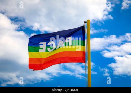 Die Flagge in den Farben des Friedens flattert vor dem Hintergrund eines wolkigen blauen Himmels. Symbol des Friedens in dieser Zeit des Krieges. pro concordia Arbeit Stockfoto