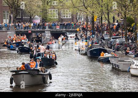 Menschen, die auf den Booten in den Grachten von Amsterdam während der Feier zum Königstag gesehen wurden. Der Königstag, bekannt als Koningsdag, ist ein orangefarbenes Fest zum Geburtstag des Königs, ein Nationalfeiertag voller Veranstaltungen im ganzen Land. Tausende von Einheimischen und Touristen besuchten Amsterdam, um an den Kanälen zu feiern und zu feiern, während sie orangefarbene Kleidung trugen und die Boote eine Parade in den Wasserkanälen machten. Stockfoto